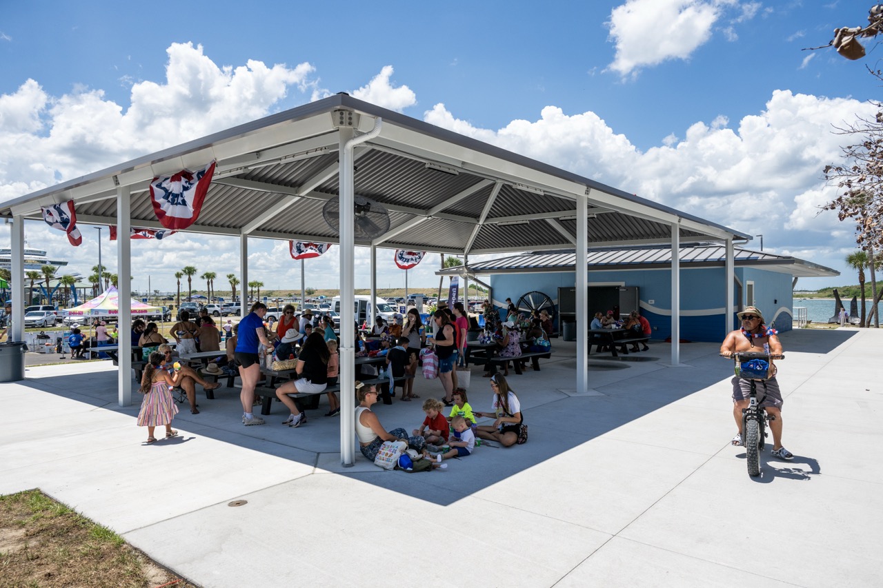 Jetty Park patrons gather at picnic tables under the shade of a pavilion to eat.