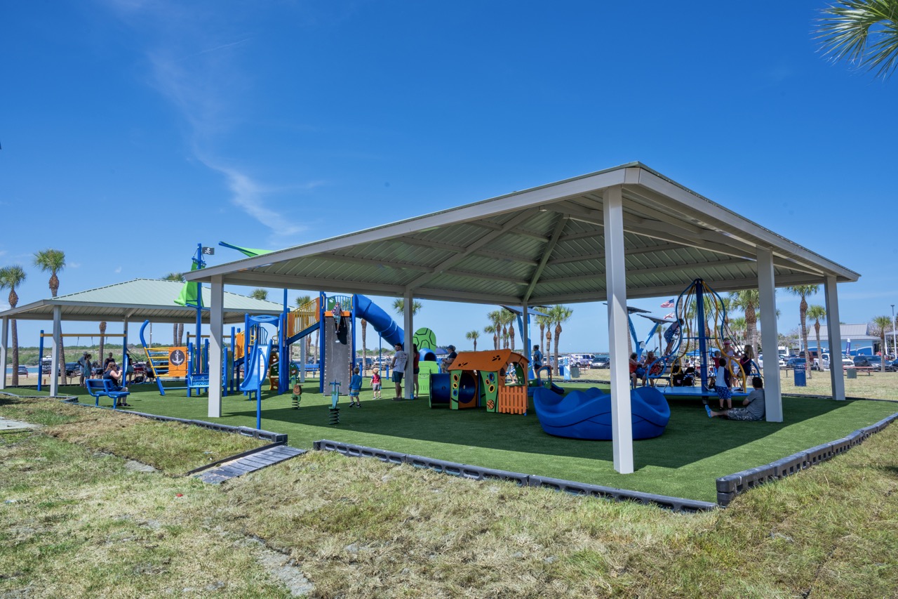 A brand new Jetty Park playground is bustling with families playing on shaded equipment.